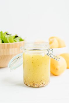 a glass jar filled with dressing next to lemons and lettuce on a white surface