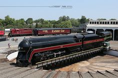 a black and red train engine sitting on the tracks next to another train at a station