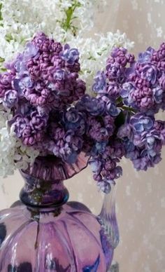 purple and white flowers are in a glass vase on a table with a wallpaper