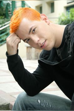 a young man with red hair and black shirt sitting on the ground looking at the camera