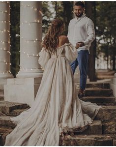 a man standing next to a woman in a white dress on some steps with lights