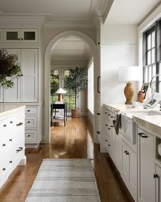 a long narrow kitchen with white cabinets and wood floors, along with an area rug on the floor