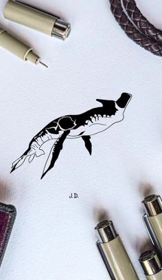 an ink drawing of a fish on paper next to some fountain pens and other office supplies