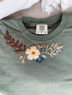 a t - shirt with an embroidered flower and leaves on the front, next to a scarf