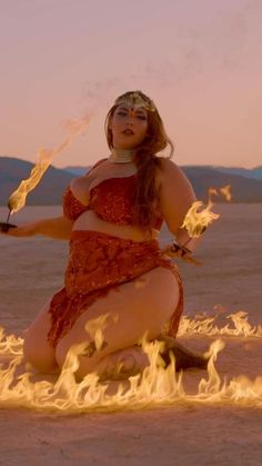 a woman sitting on the ground with fire in her hand and wearing a headdress