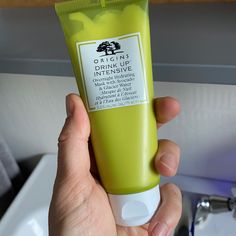 a person holding up a tube of green toothpaste in front of a sink