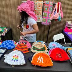 a woman standing in front of a table filled with crocheted hats