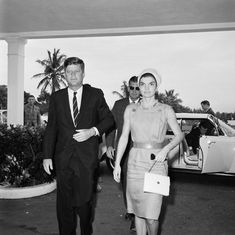 black and white photograph of man and woman walking in front of an entrance to a hotel