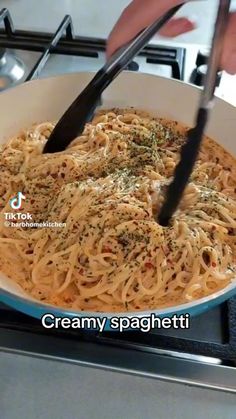 someone is stirring some noodles in a skillet on the stove with black tongs