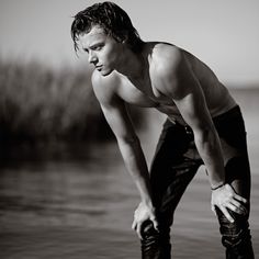 a shirtless man standing in the water with his hands on his knees and looking down