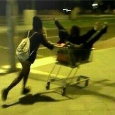 a woman pushing a man in a shopping cart on the sidewalk with a message written below