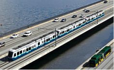 a blue and white train traveling over a bridge next to the ocean with cars driving on it