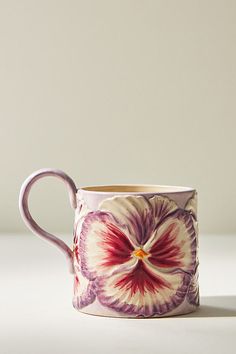 a pink and purple flower mug sitting on top of a white table next to a wall