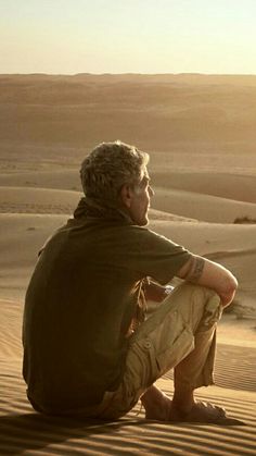 a man sitting on top of a sandy dune