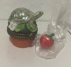 a turtle figurine sitting on top of a flower pot next to a tomato