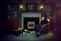 a man sitting on a chair in front of a fire place with paper scattered around him