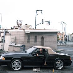 a man sitting in the driver's seat of a black sports car on a city street