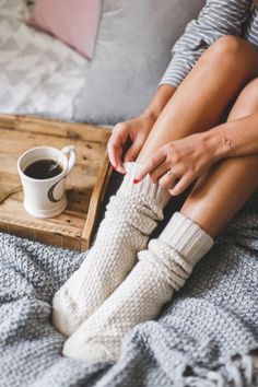 a woman sitting on top of a bed next to a cup of coffee