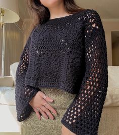 a woman wearing a black crochet sweater and skirt standing in front of a couch