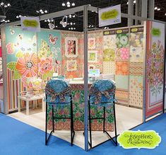 a booth at a craft show with colorful fabrics on the walls and chairs in front