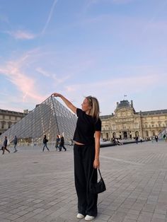 a woman standing in front of a pyramid pointing at the sky with her hand up