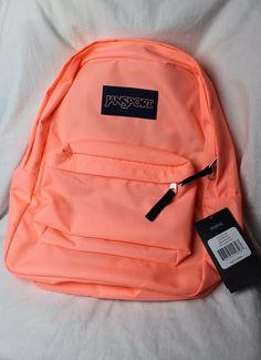 an orange backpack sitting on top of a white bed next to a tag that says jansport