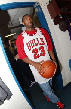 a man holding a basketball in his right hand while standing next to a wall with other people