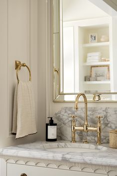 a bathroom with marble counter top and gold faucet, white cabinetry and mirror