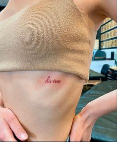 a woman's stomach with the word divine tattooed on her left side ribcage