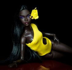 a doll with long black hair wearing a yellow swimsuit and flower in her hair