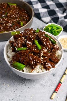 two bowls filled with beef and rice on top of a table next to chopsticks