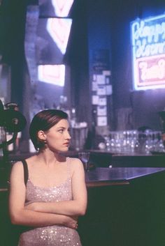 a woman standing in front of a bar with her arms crossed and looking off to the side