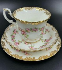 an antique tea cup and saucer with gold trimmings on the rim, decorated with pink flowers
