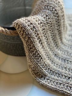 a close up of a knitted blanket on top of a white table cloth next to a pot