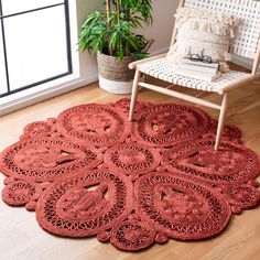 a red rug is on the floor in front of a chair and potted plant