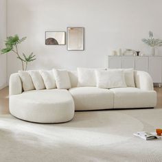 a living room with a large white couch in the center and potted plants on the floor