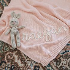 a knitted bunny laying on top of a pink blanket with the word reagan written across it