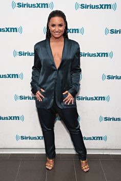 a woman standing in front of a wall wearing a black suit and gold heels with her hands on her hips