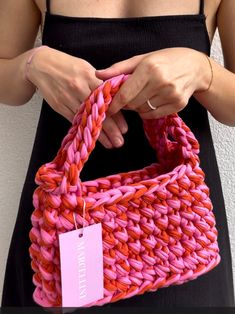 a woman is holding a pink and red bag with a tag on it's handle