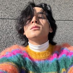 a man with black hair wearing a multicolored sweater looking up at the sky