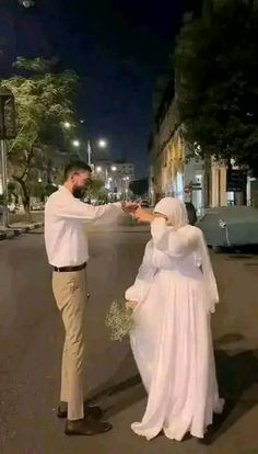 a man and woman dressed in white standing next to each other on a street at night