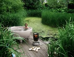 a woman sitting in a large bathtub next to a pond with marsh and reeds