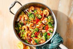 a pan filled with shrimp and broccoli next to lemon wedges on a table