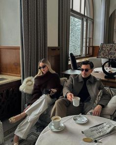 a man and woman are sitting on a couch in a living room with large windows