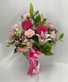 a vase filled with lots of pink flowers and greenery next to a white wall