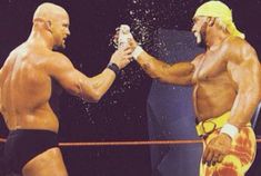 two men standing next to each other in front of a wrestling ring with water pouring on them
