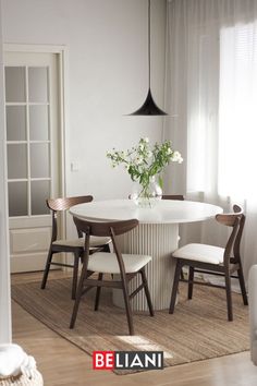 a white table with four chairs around it and a vase filled with flowers on top