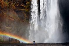 a person standing in front of a waterfall with a rainbow