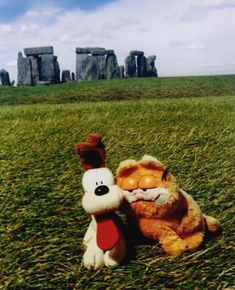 a stuffed animal is sitting in the grass next to a teddy bear that looks like it's hugging him