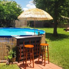 an above ground pool with two stools next to it and umbrella in the background
